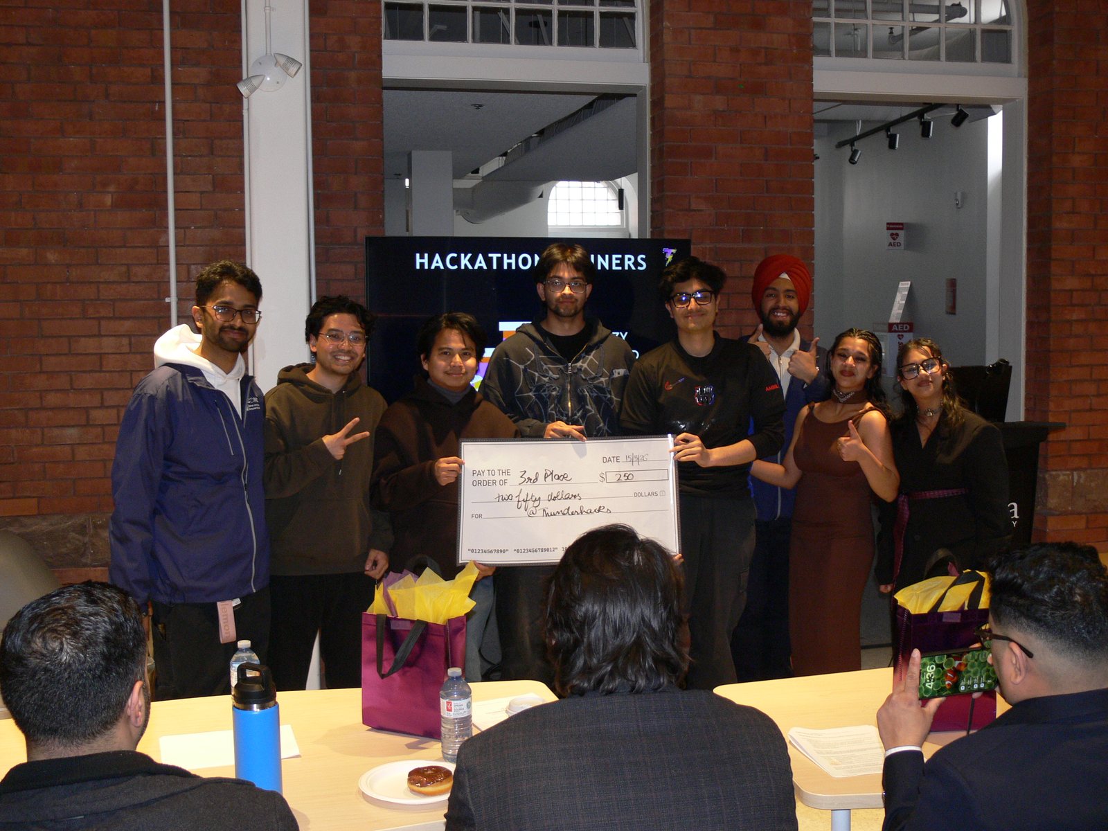 A winning team holding an oversized prize cheque in front of the hackathon winners screen at ThunderHacks, March 2026